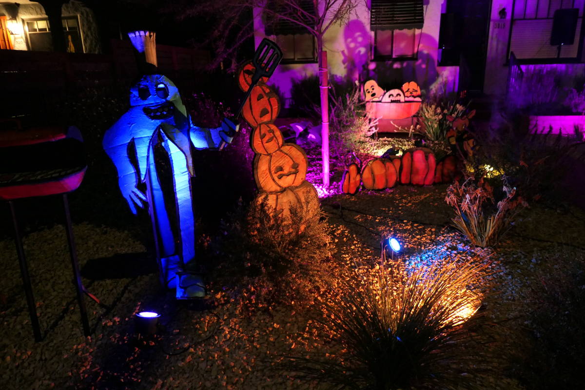 A wider shot of the ghost with the grill as well as lots of pumpkins. Behind a bush is a faun-like creature considering which of two pumpkins is less suspicious.